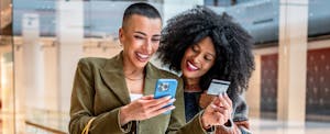 Two young women shopping online using a credit card in a mall.