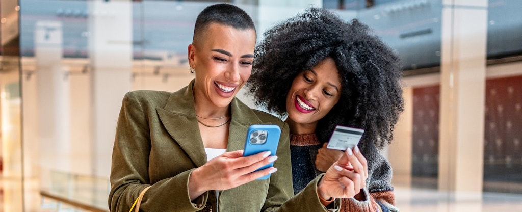 Two young women shopping online using a credit card in a mall.