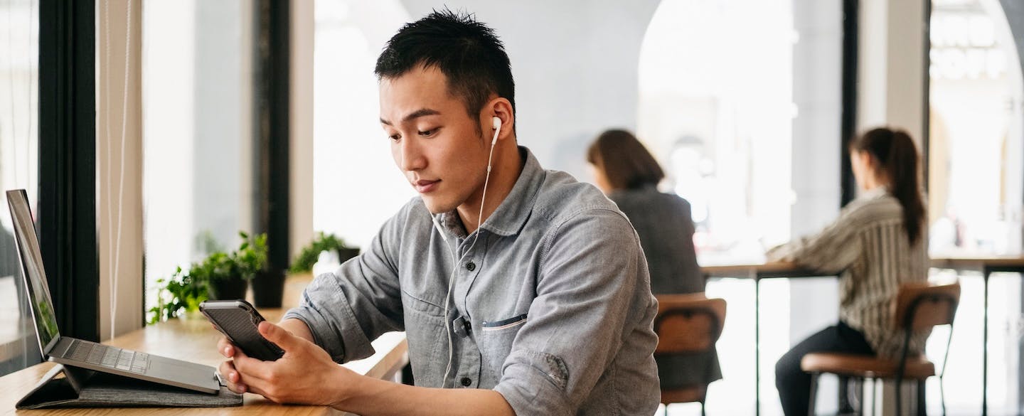 Freelance worker wearing earphones and text messaging on smartphone