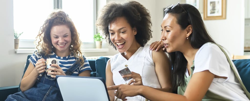 Three multi-ethnic young women shopping online while sitting on the sofa in the living room.