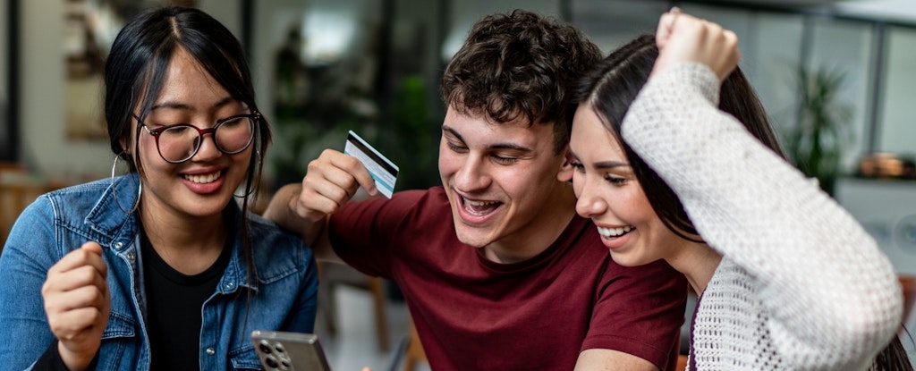 Multiracial group of friends with a credit card and phone, enjoying time together in a cafe.