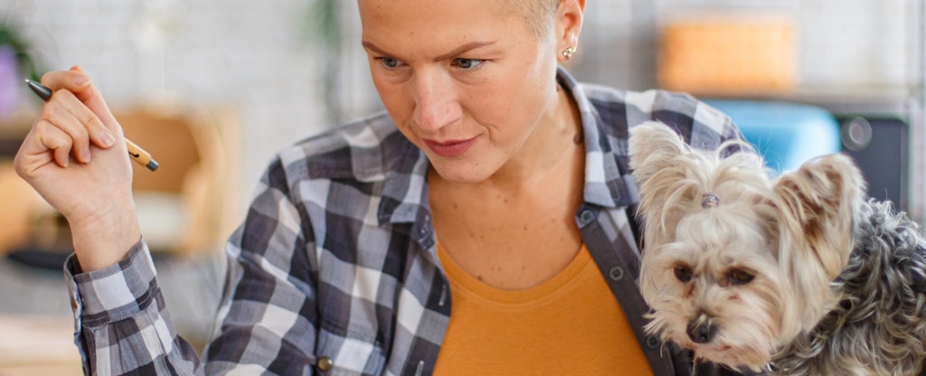 Woman working from home while her dog sits on the desk.