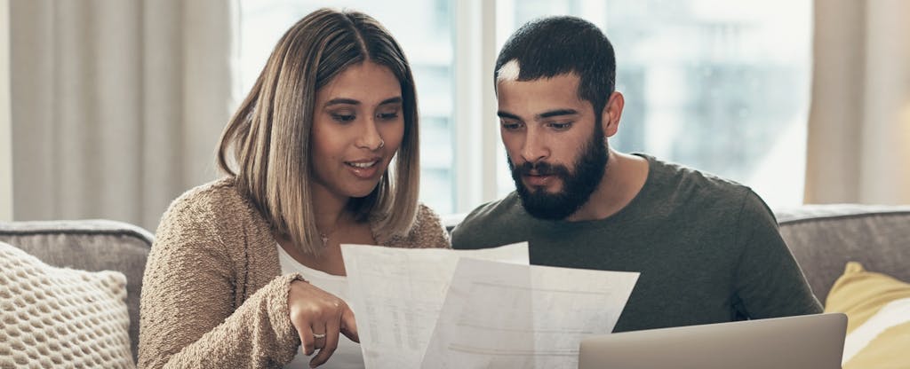 A man and woman couple using a laptop while going through paperwork at home.