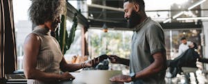 A man with a beard pays the receptionist at his barbershop using his credit card.