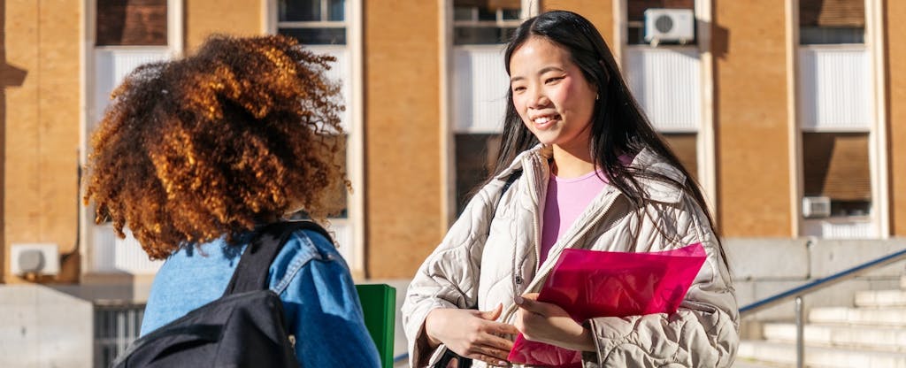 Two young adult university students having a conversation on campus, sharing and discussing while walking between classes
