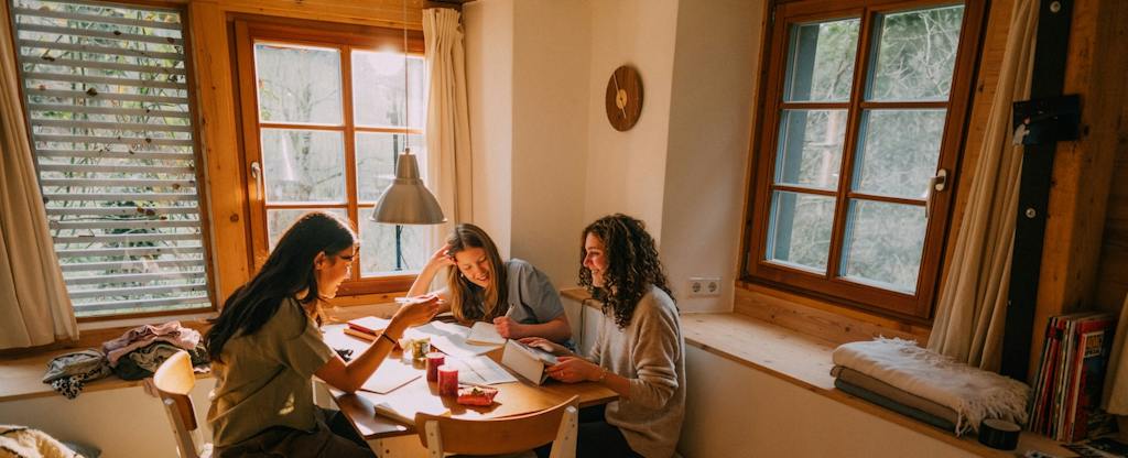 car-insurance-with-bad-credit Three friends gather around a wooden table in a warm, sunlit cabin to study, review papers, and share ideas.